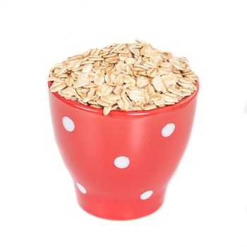 red cup with oats flakes pile on white background.
