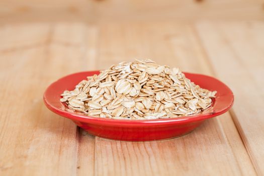 red dish  with oats flakes pile on wood background.