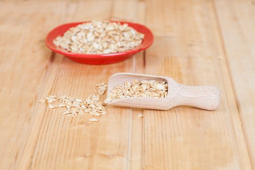red dish and wood spoon with oats flakes pile on wood 
background.
