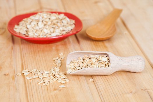 red dish and wood spoon with oats flakes pile on wood 
background.