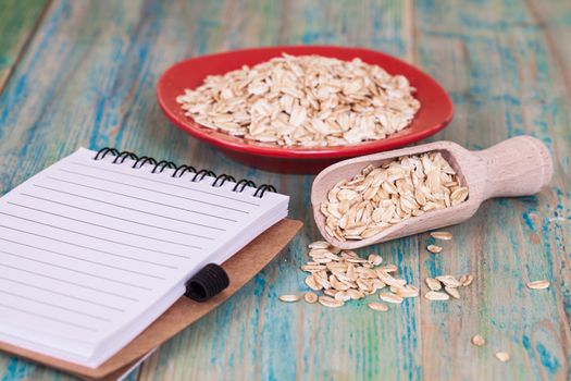 red dish and wood spoon with oats flakes pile and book note