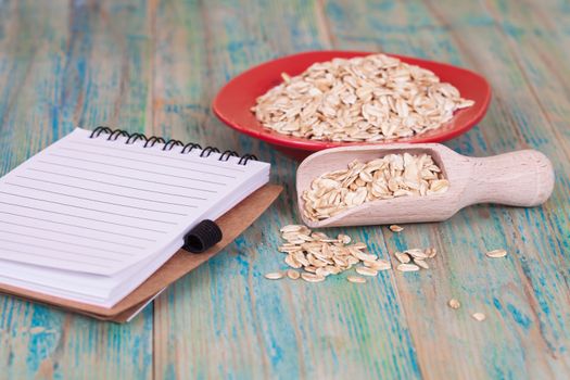 red dish and wood spoon with oats flakes pile and book note