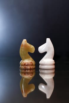 Opposition concept. Two chess horses made from Onyx against dark background