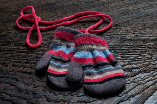 two knitted striped baby mittens on wood background