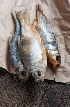 Salty dry river fish is on crumpled yellow paper  on a brown wooden background 