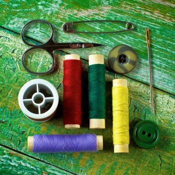 Arrangement of Various Spools of Thread, Scissors, Pins, Needles and Buttons closeup on Cracked Wooden background