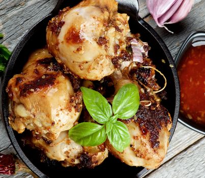 Delicious Spicy Roasted Chicken Legs with Herbs, Sauce and Spices in Black Frying Pan on Rustic Wooden background. Top View