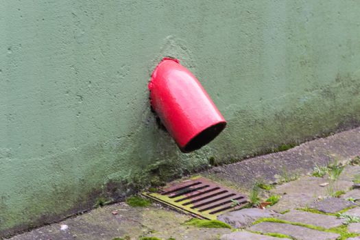 Rainwater drain. Old red gutter downpipe with weathered dirty metal frame.