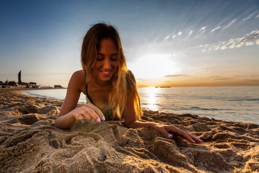 attractive sexy woman in bikini laying on sand on lonely beach on sunrise