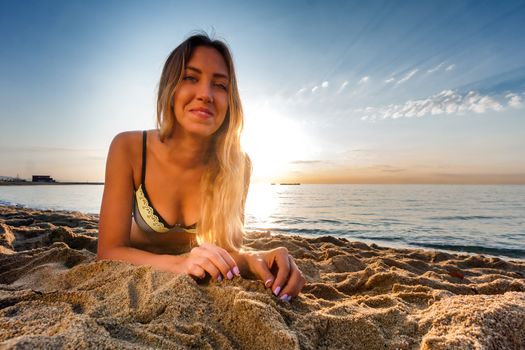 attractive sexy woman in bikini laying on sand on lonely beach on sunrise time