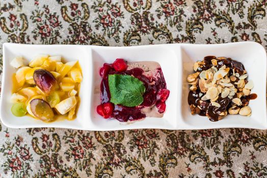 sliced fruits, nuts and ice cream with fruit and chocolate sauce in white saucers