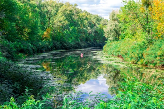Sunny landscape of river, greenwood forest, and cloudy sky reflected in water