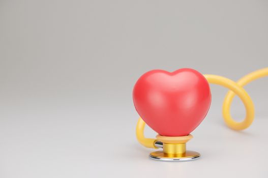 Red heart on yellow and gold stethoscope and swirl rubber tube with white background.