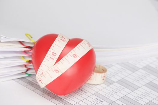 Red heart with measuring tape on finance account have blur pile paperwork of receipt and report with colorful paperclip as background.