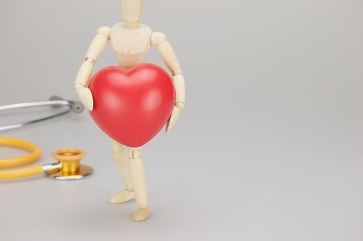 Wooden dummy holding red heart have blur yellow and gold stethoscope on white background.