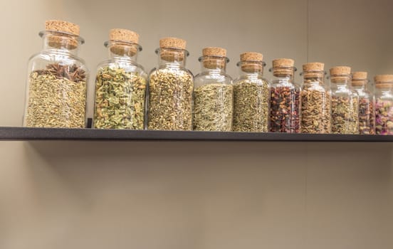 Glass bottles with different dry tea ingredients, placed on a rack