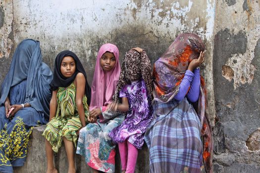 Stone Town, Tanzania - January 10, 2016: Children in traditional Muslim clothes sitting on the street of Stone Town.