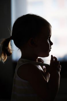 Silhouette of todler girl alone in the front of a window