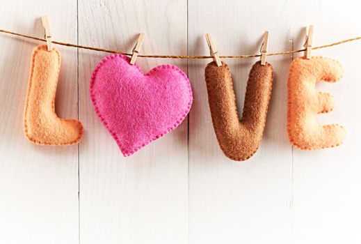 Love, Valentines Day. Word Love, Heart Handmade, hanging on rope. Vintage romantic style, white wooden background, toned. Vivid unusual creative greeting card, multicolored felt