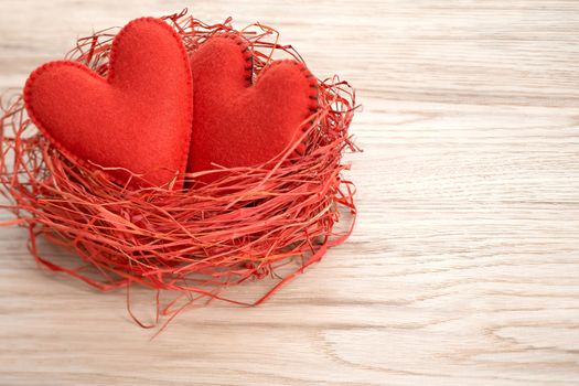 Love hearts, Valentines Day. Hearts handmade on wooden background. Couple made of red felt in straw nest. Vintage romantic style. Vivid greeting card, copyspace.  