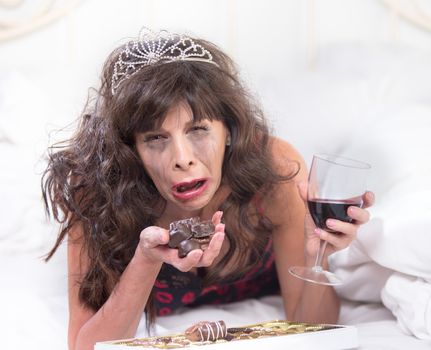Sobbing mature woman wearing a tiara crying and cramming chocolates in her bedroom