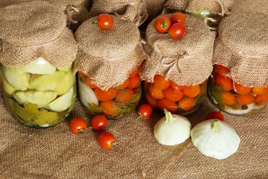 Transparent banks with marinated Cherry tomatoes and baby summer squash. Home canning. Banks pickled tomatoes