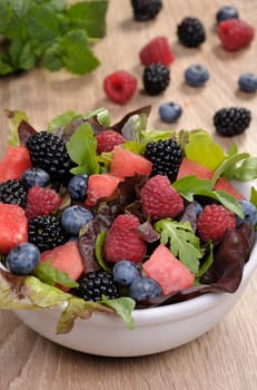 Fruit salad with blackberry, raspberry, blueberry, watermelon slices and mix of green leaves
