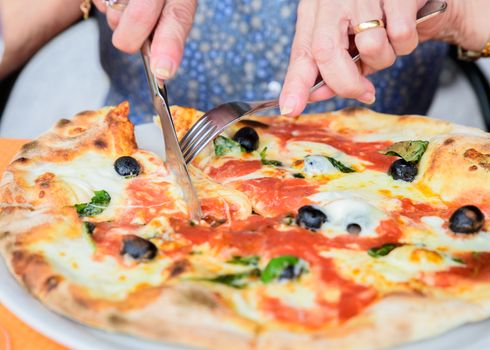 Close-up of woman hands cutting pizza outside at restaurant, selective focus.