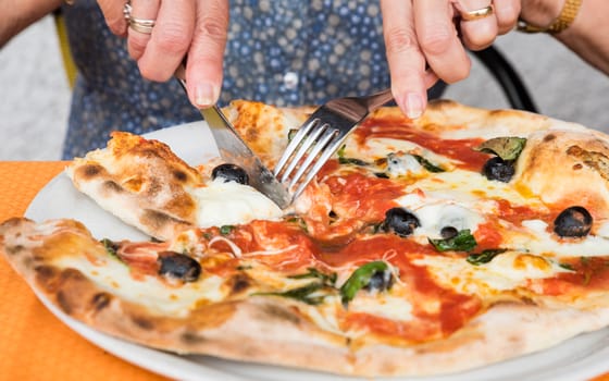 Close-up of woman hands cutting pizza outside at restaurant, selective focus.