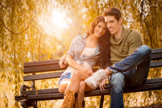 Beautiful young couple sitting on a bench in the park, enjoying and looking away.