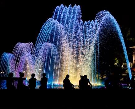 Night colored fountain with silhouettes of people.