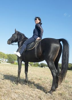 beautiful girl riding a black stallion in a field