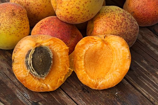 Few ripe orange whole apricots and one cut in half into a rough wooden background. Summer fruit background. Close-up image