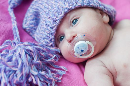 Little baby with soother in hat lays