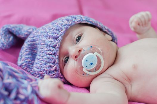 Little baby with soother in hat lays