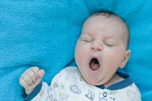 Little baby yawns on the blue towel