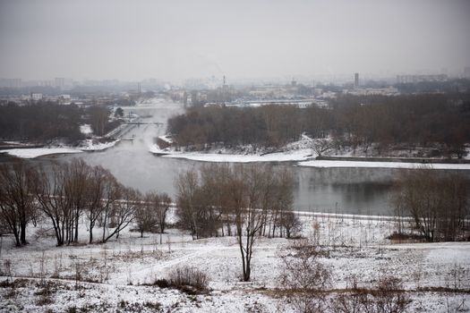 River fog at dawn. winter panorama near the river, Russia. Winter landscape of snow-covered fields, trees and river in the early misty morning. Thermal power plant with smoking chimneys on the river / ecology.