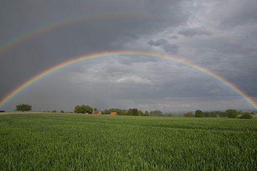 Natural rainbow over green field and dark sky