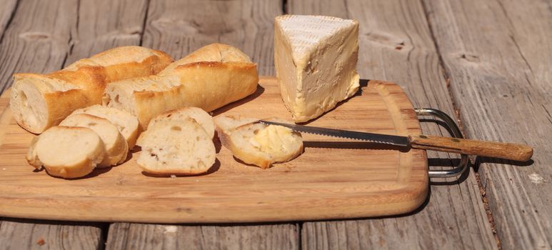 French bread and triple cream brie cheese on a cutting board with a knife.