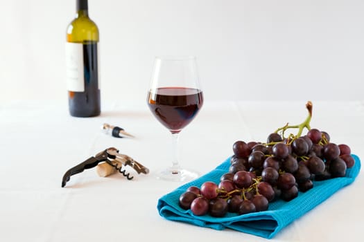Bunch of red grapes and a glass of red wine with a wine bottle on a white tablecloth