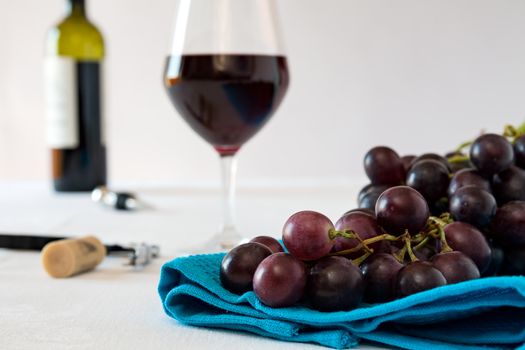 Closeup of a bunch of red grapes and a glass of red wine with a wine bottle on a blue tablecloth