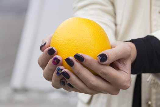 Bright, fresh orange in the hands of the girl with the fashionable manicure