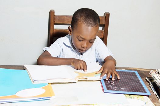 This child is studying at home with his reading book, his slate and his sketchbook.