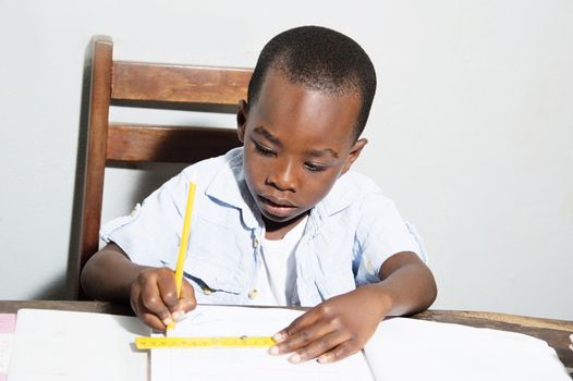 Child draws a line in pencil with a wooden ruler.