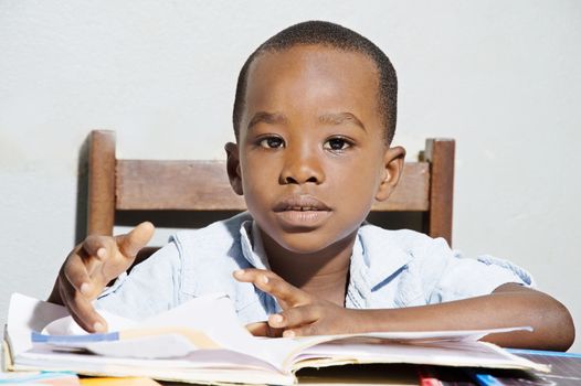 This child sitting on a chair , his reading book in front of him, looking in the camera objective.