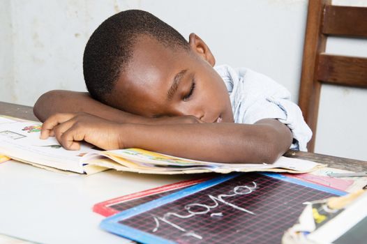 This child tired of studying , sleeping on his study table with his head in his book.