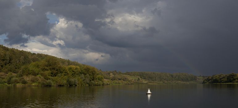 Panorama of the river with clouds and a rainbow after the rain.