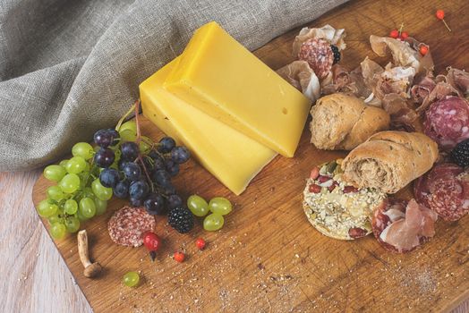 Fresh grapes, cheese bacon berries and salami on wooden table