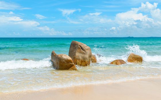 Clear azure sea crashing on rocks on tropical sandy beach