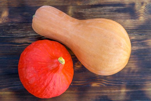 Red pumkin and yellow calabash  with hard rind laying diagonally on dark brown wooden background